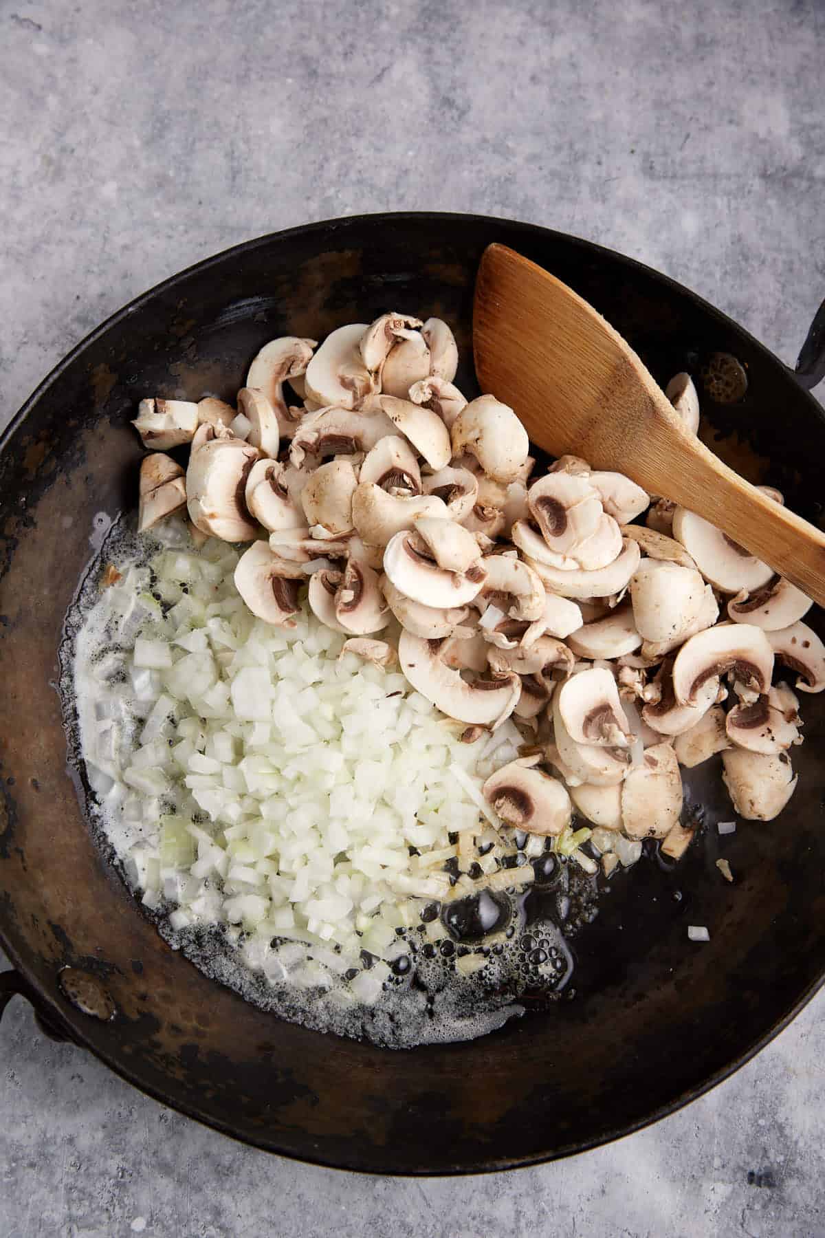 Raw onions and mushrooms in a skillet.