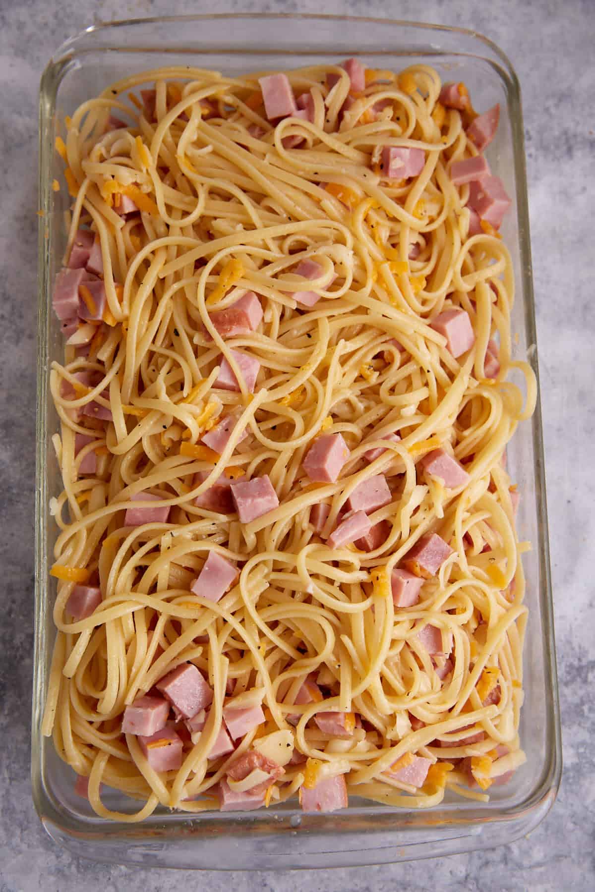 A mixture of pasta ham and cheese in a casserole dish.