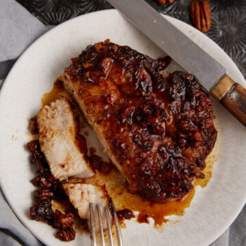 A honey glazed pork chop on a plate with a knife and fork.
