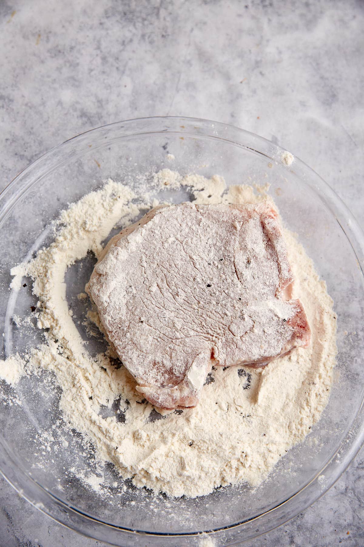 A pork chop being dredged in flour.