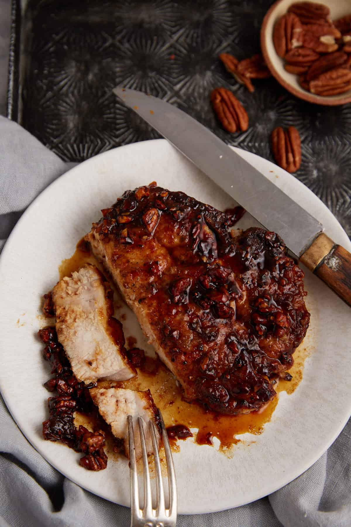 A pecan honey glazed pork chop on a plate with a fork.
