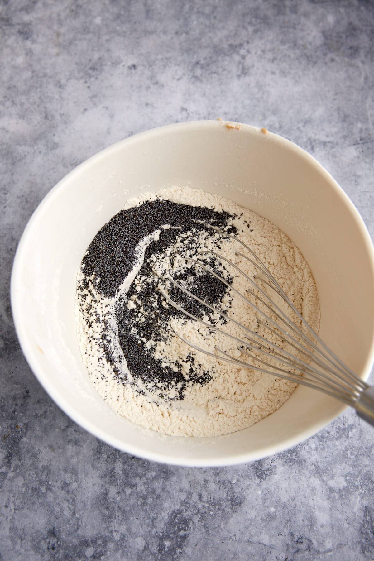 Poppy seeds added to flour mixture in a bowl.