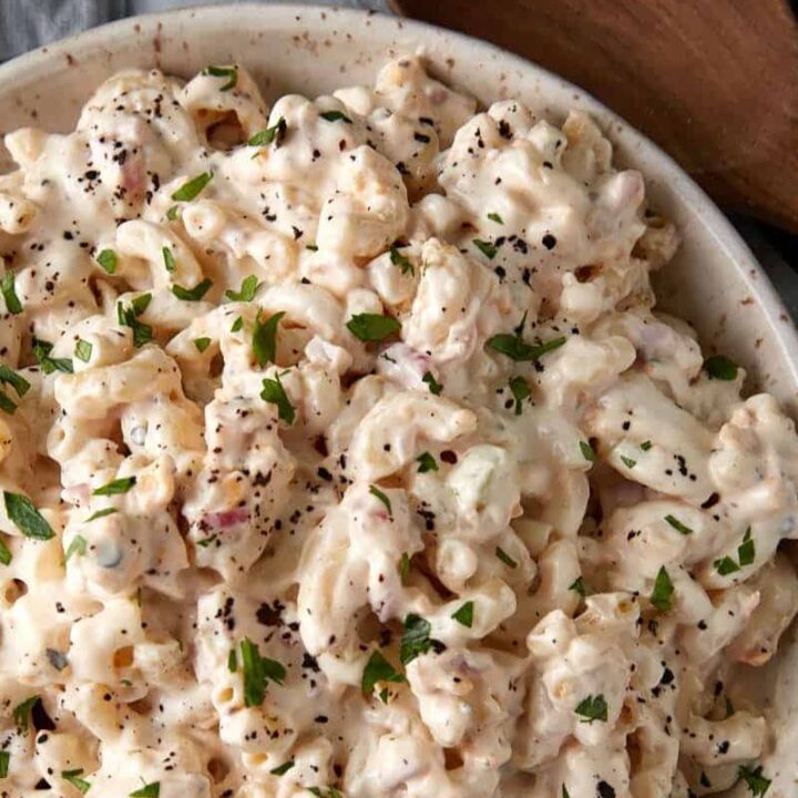 A bowl of macaroni Salad next to a wooden spoon.
