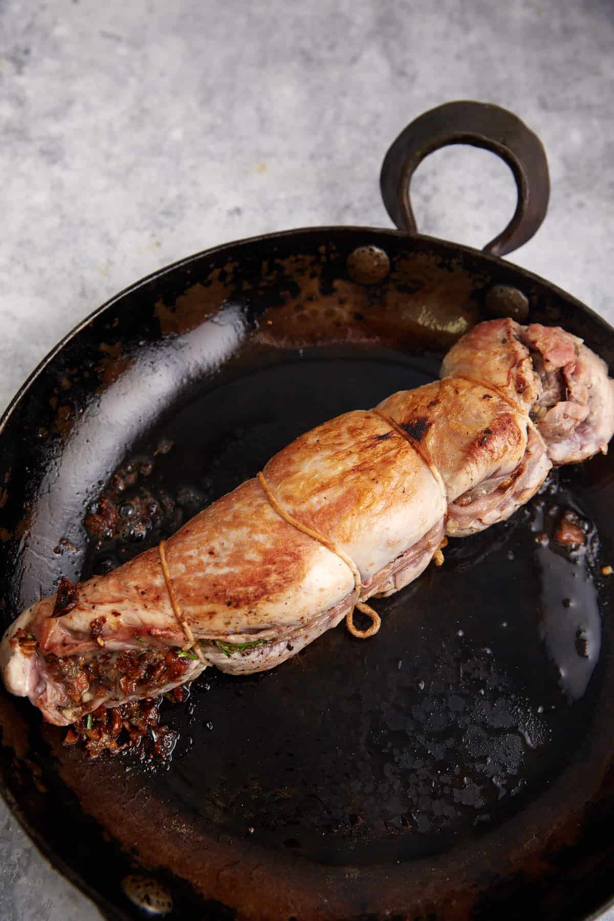 A pork tenderloin browned in a skillet.