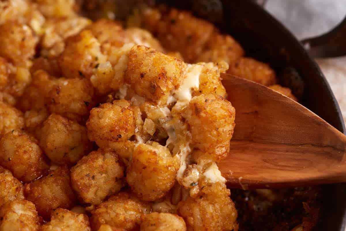 A wooden spoon in a skillet of tater tot casserole.