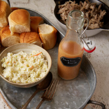 A tray with rolls, coleslaw and carolina bbq sauce.