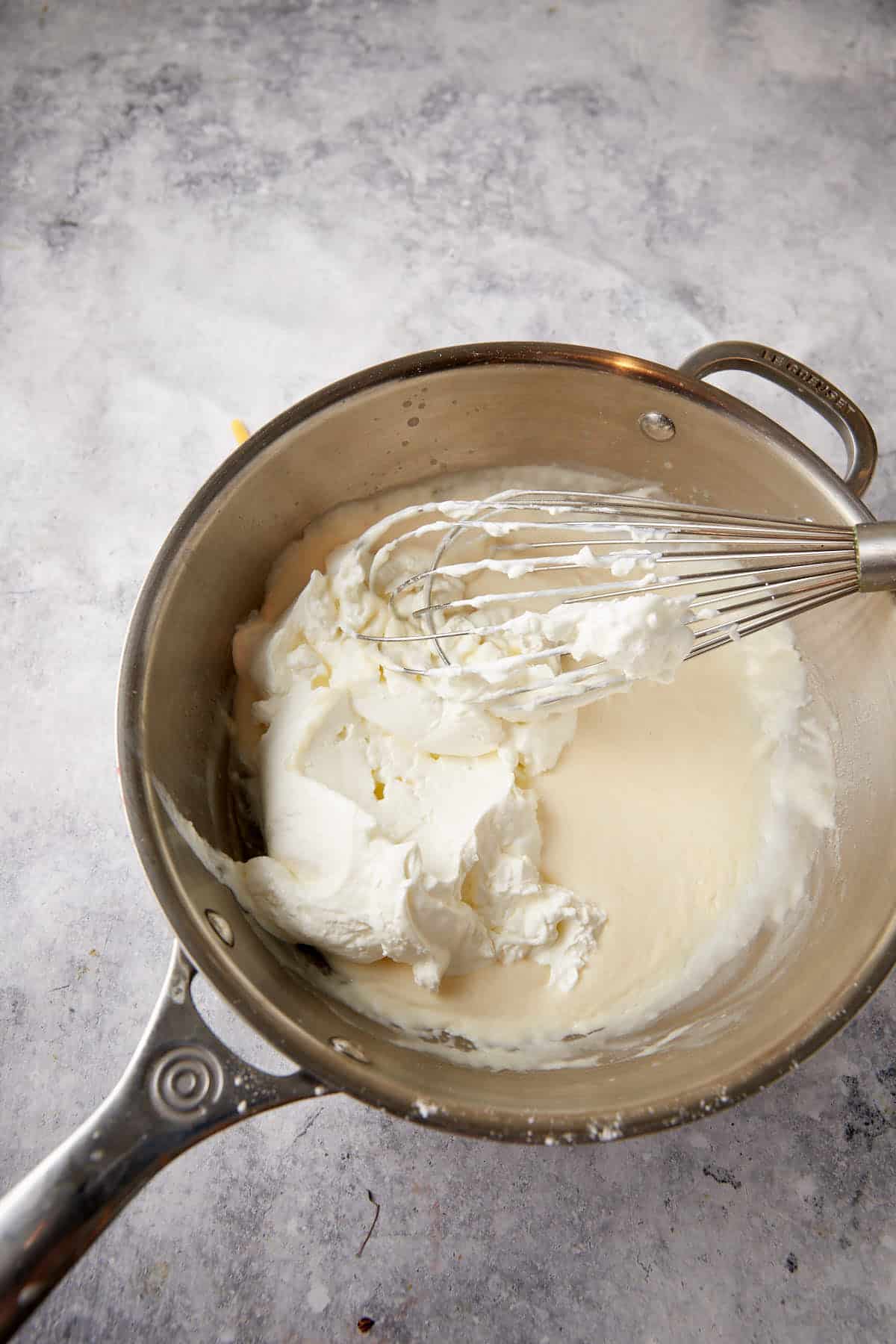 Sour cream added to a saucepan of sauce.