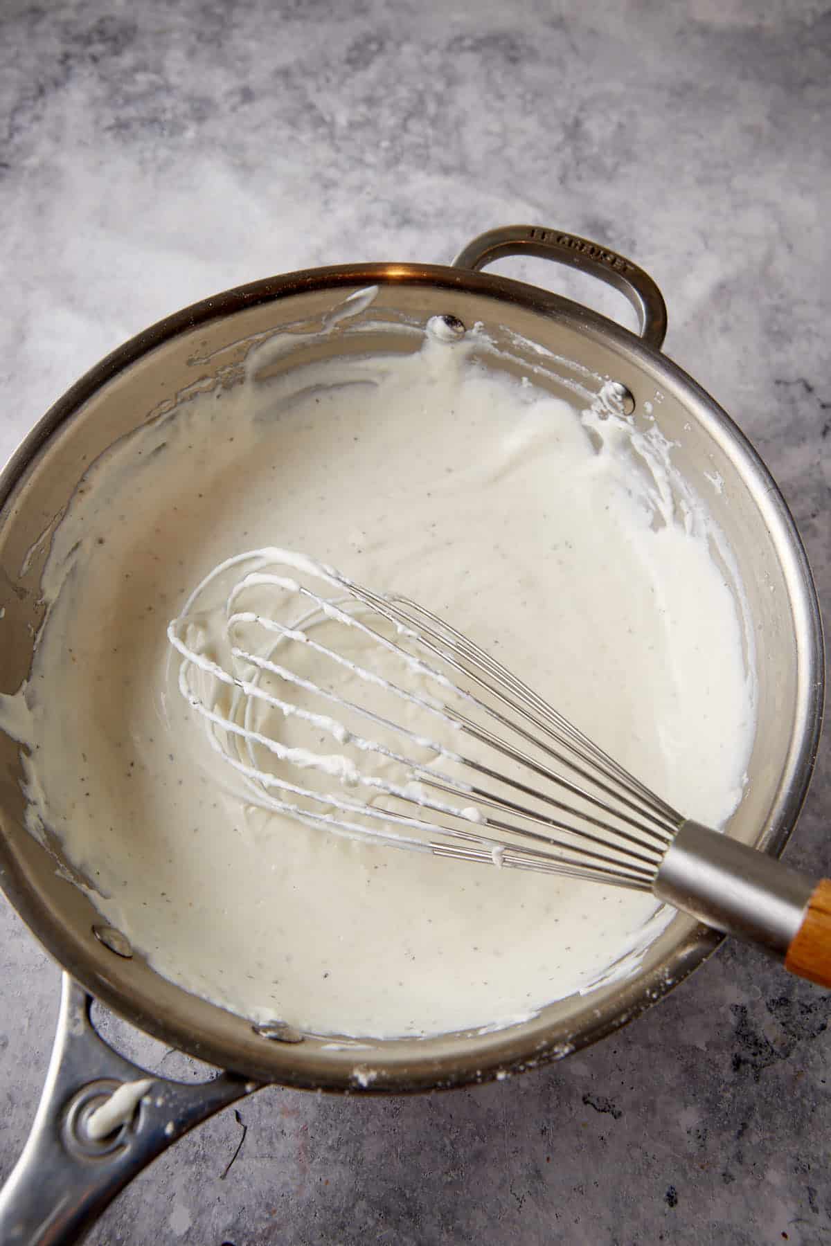 A white sauce in a skillet with a whisk.