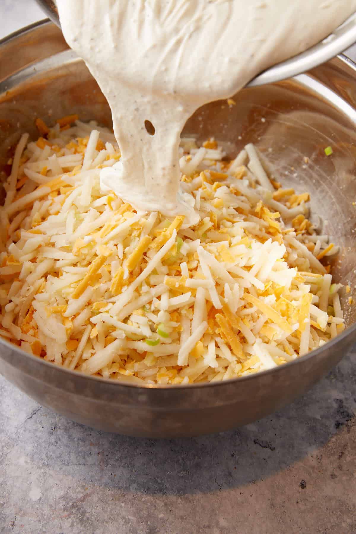 Sauce being poured over chicken and cheese and hashbrowns in a bowl.