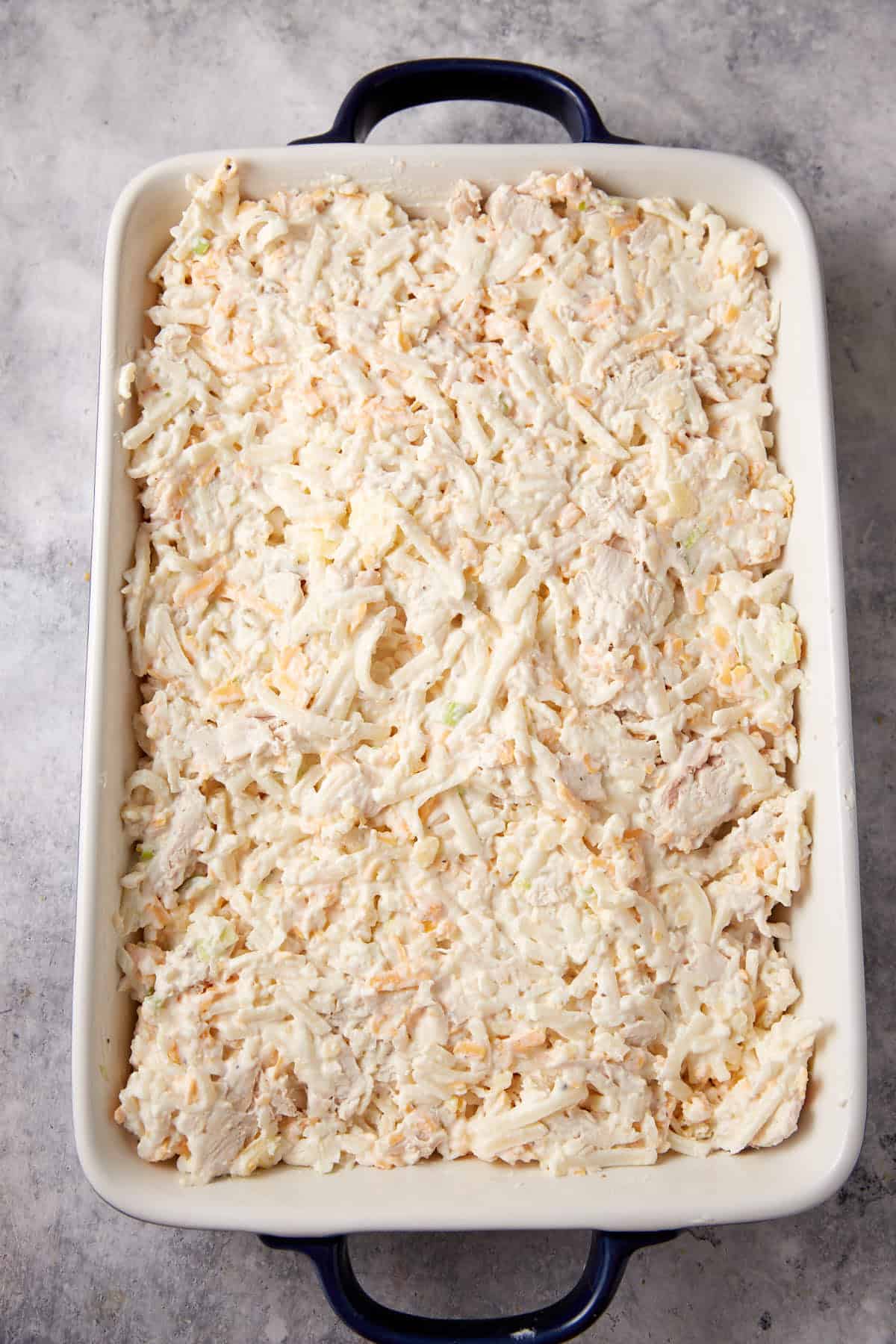 A casserole dish with an unbaked chicken and hashbrown casserole.