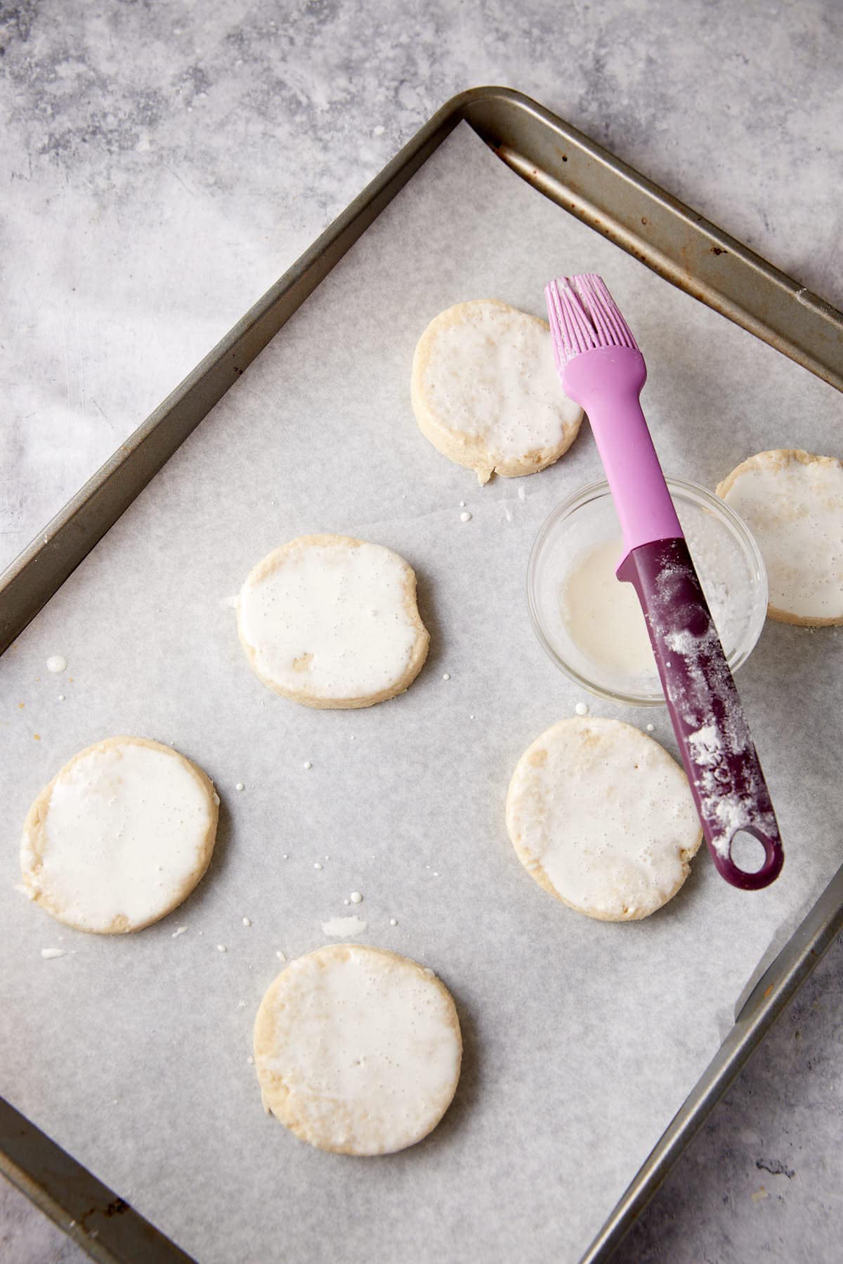 Biscuit dough on a baking sheet with cream and sugar on top.