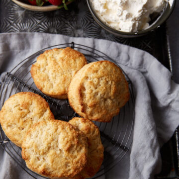A stack of biscuits on a wire rack next to strawberries and cream.