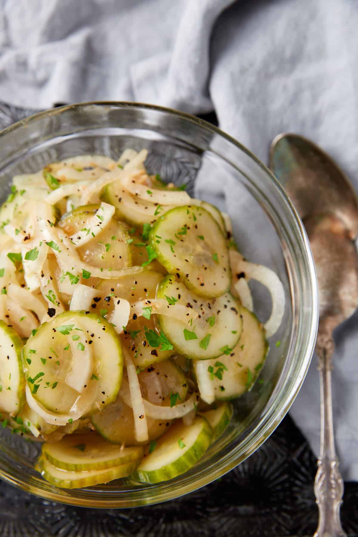 A bowl of cucumber salad with onions and two serving spoons