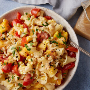 A serving bowl with a dressed peach and pasta salad.