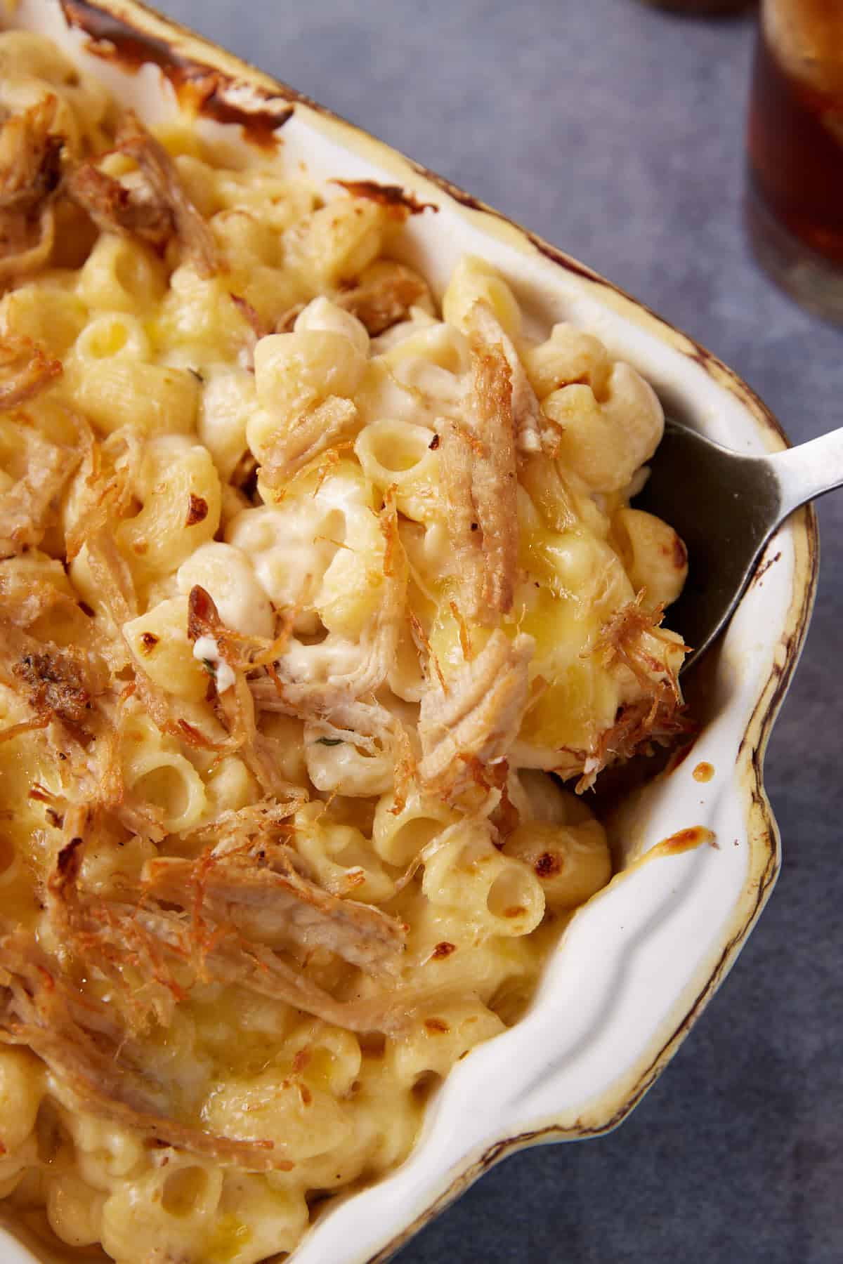A serving spoon in a casserole dish of pulled pork mac and cheese.