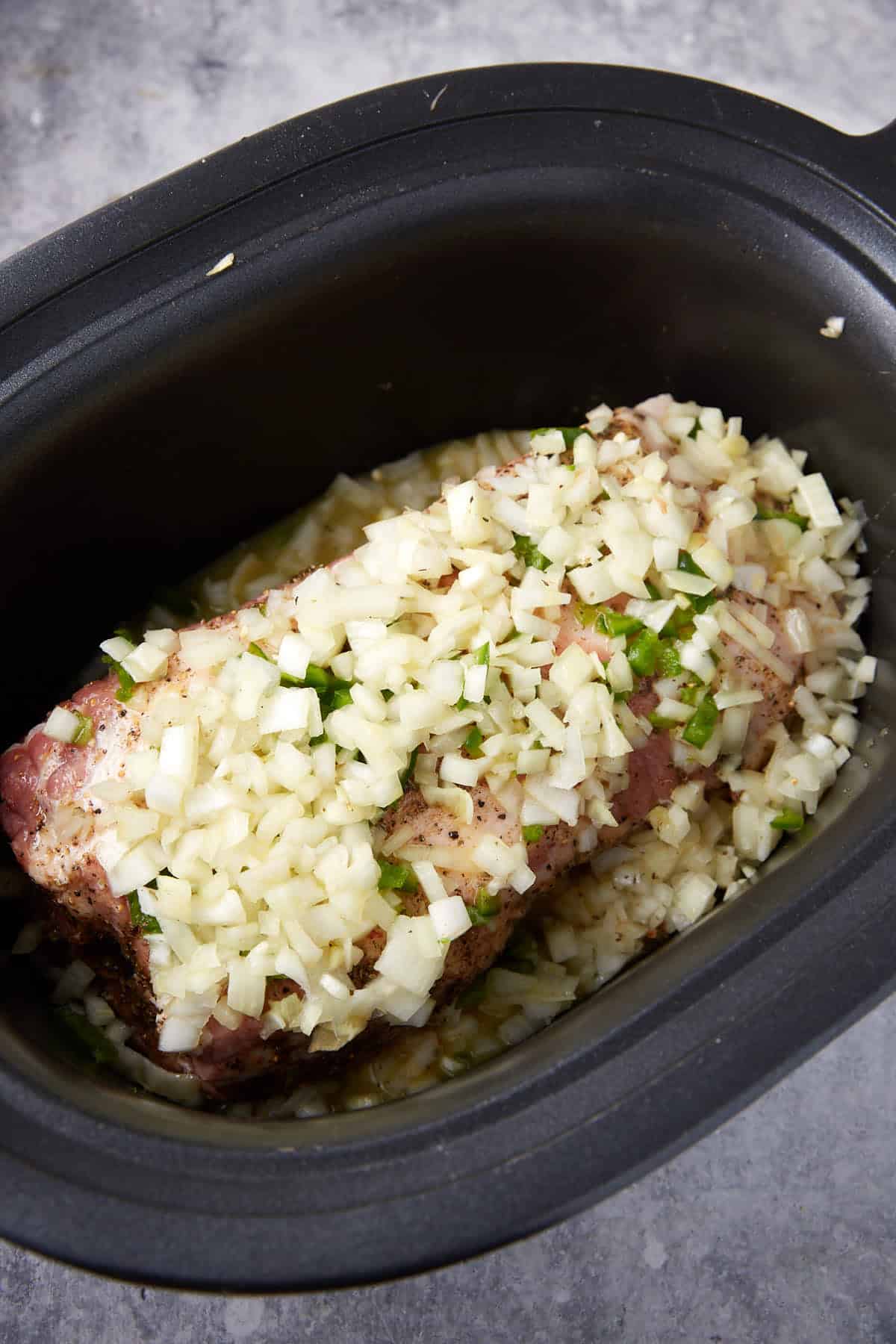 A pork shoulder in a crockpot covered with onions.