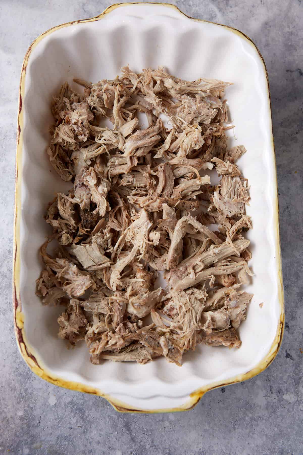 A casserole dish with cooked pulled pork on the bottom.