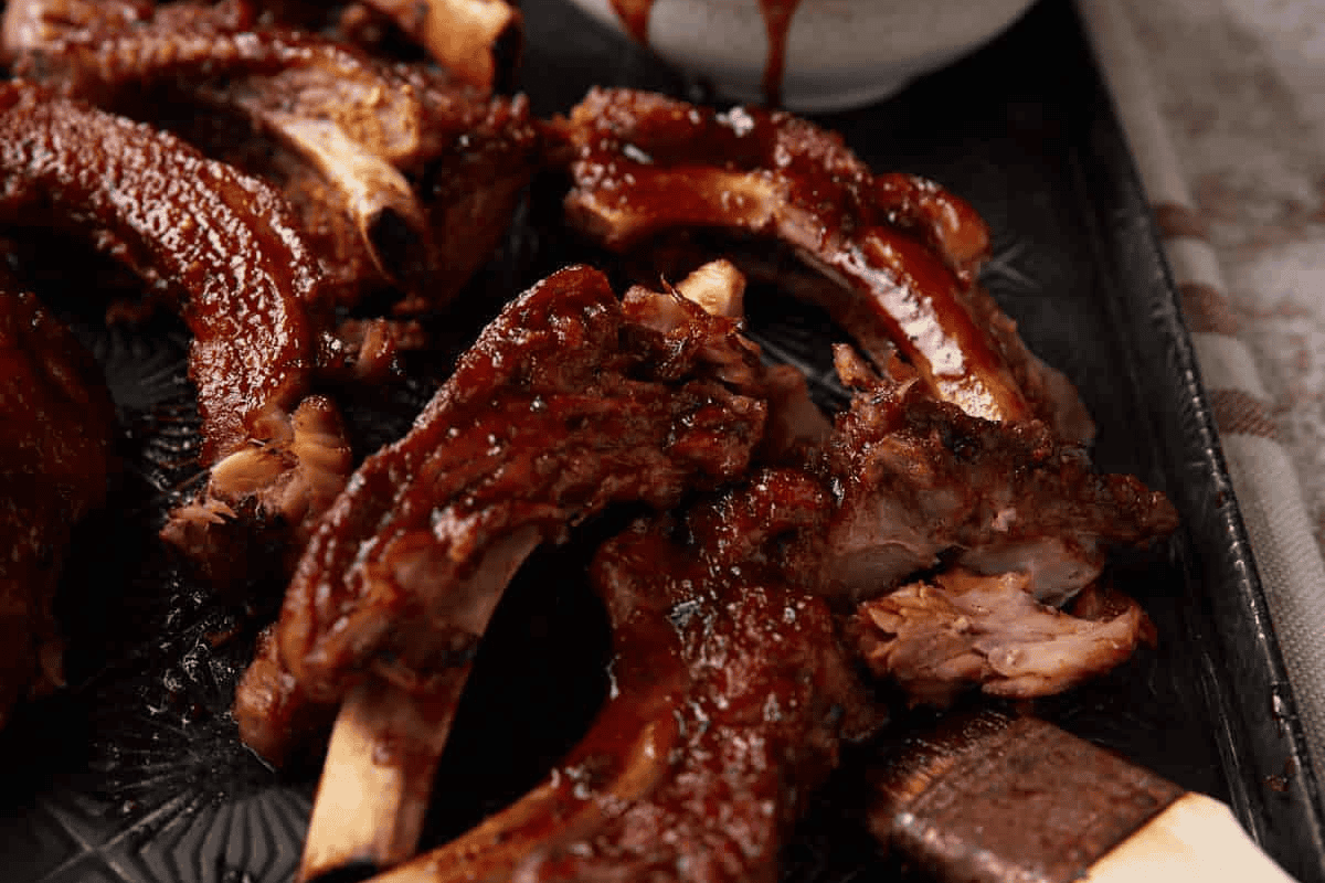 slow cooker ribs on a platter with a bowl of sauce.