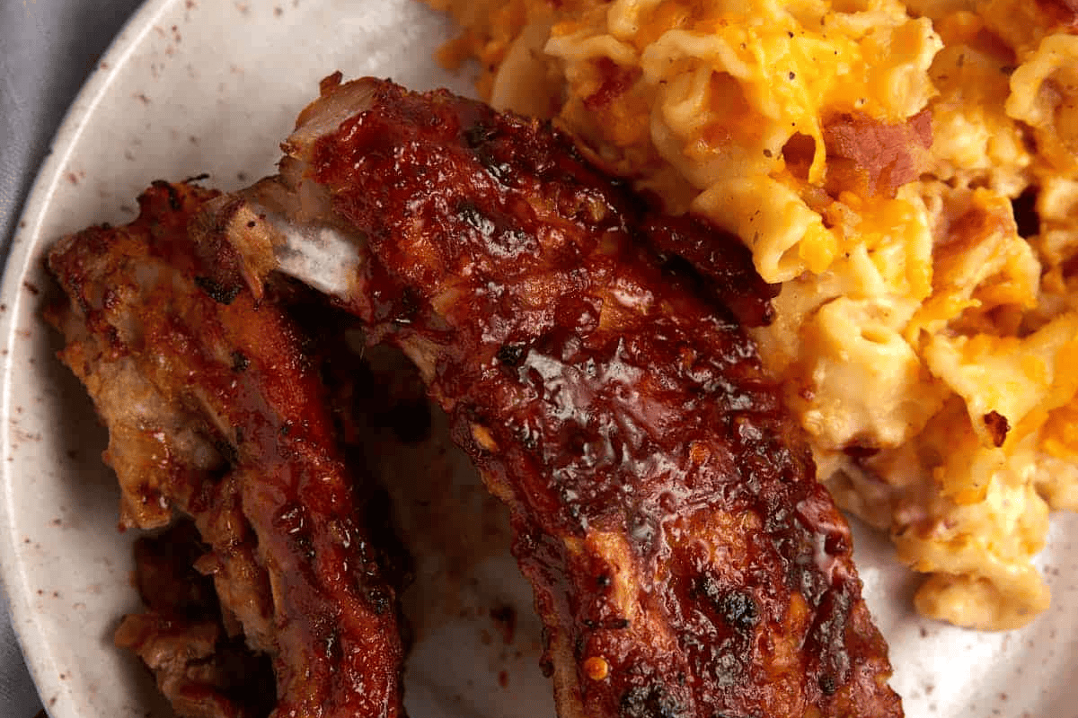 ribs on a plate next to mac and cheese.