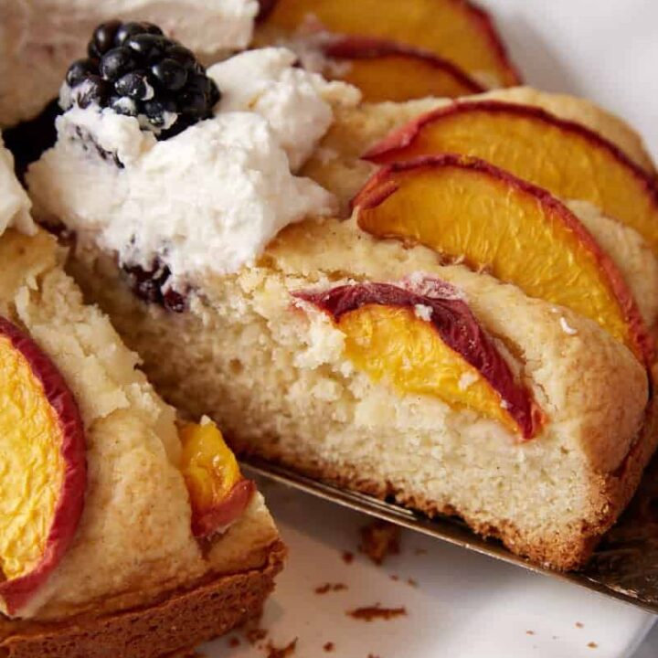 A slice of peach blackberry cake topped with whipped cream.