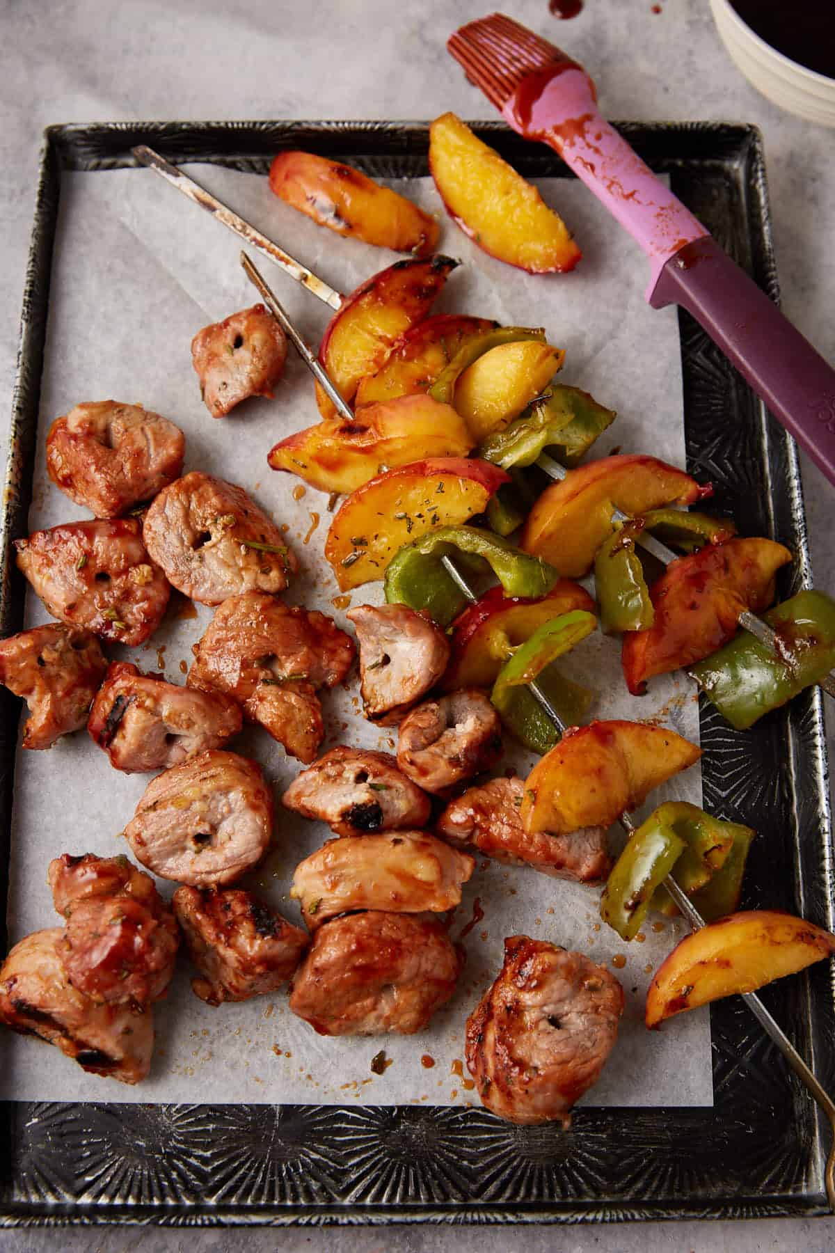 A platter with peaches on skewers next to pork pieces. 