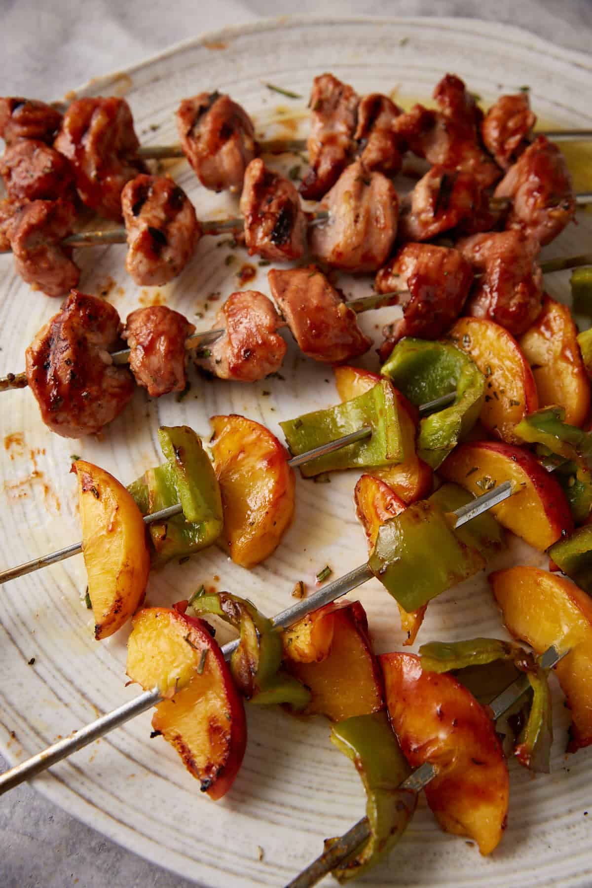 A platter with pork kabobs and peach kabobs.