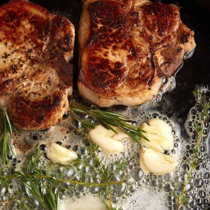 Two pork chops in a skillet with butter and garlic.