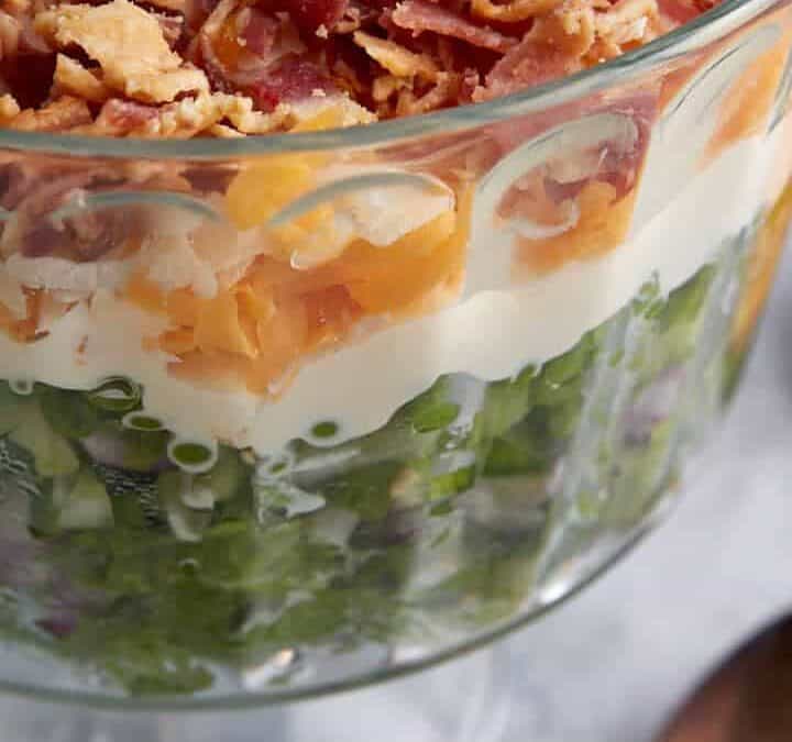 A bowl of 7 layer salad next to a serving spoon.