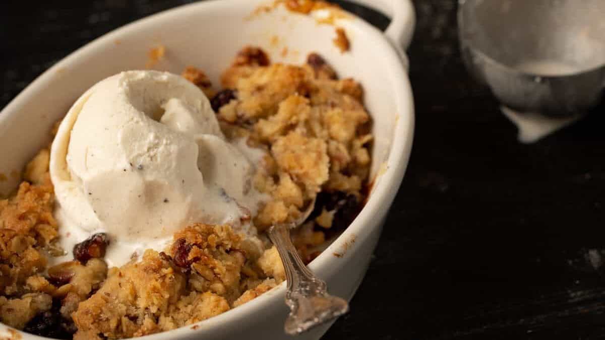 Two ramekins of apple blackberry crumble with an ice cream scoop and vanilla ice cream.