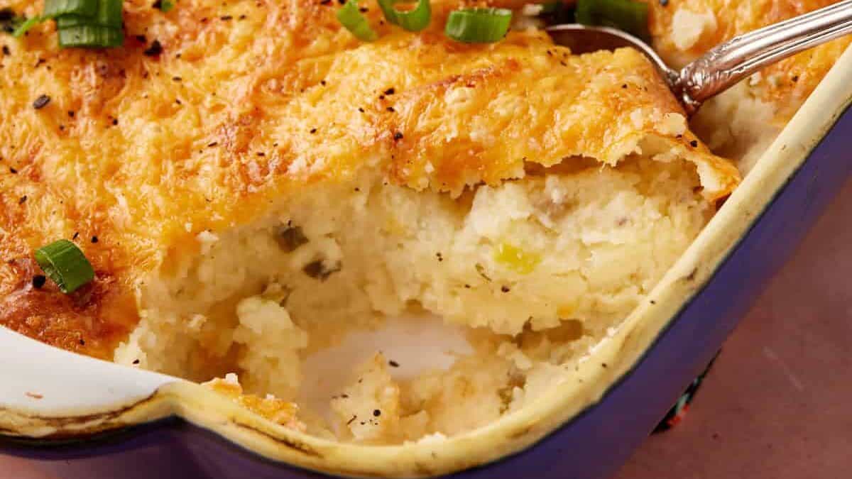 A spoon full of baked mashed potatoes in a casserole dish.