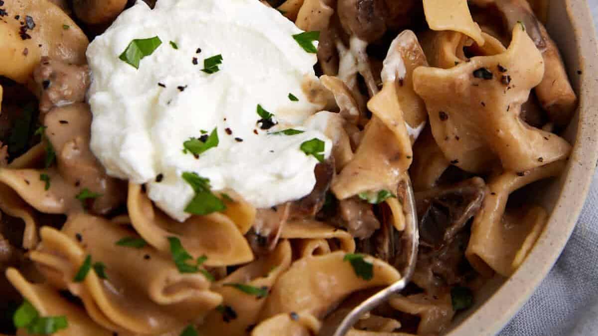 A bowl of beef stroganoff topped with sour cream.