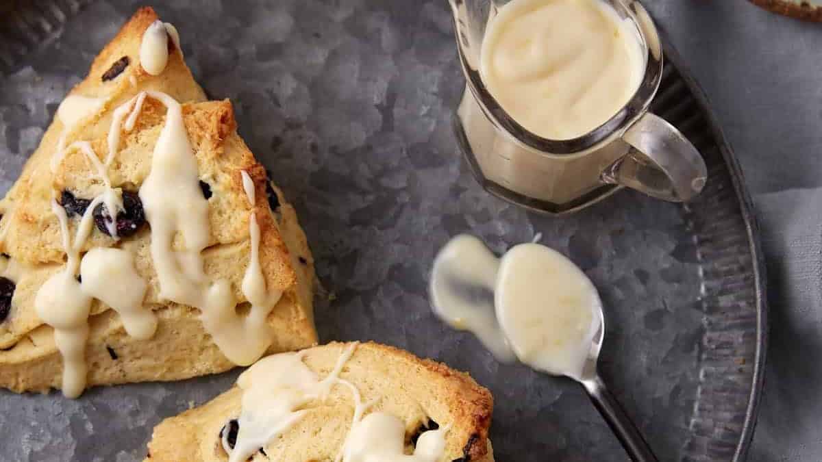 Two blueberry scones on a platter drizzled with a glaze.