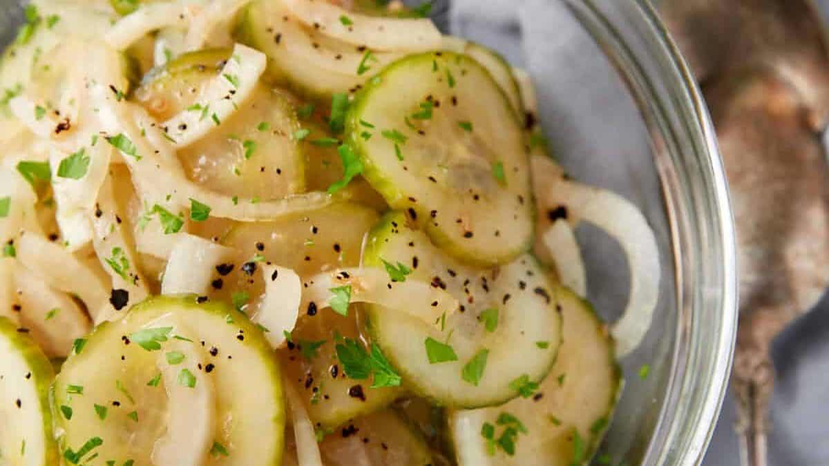 A bowl of cucumber salad with onions and two serving spoons