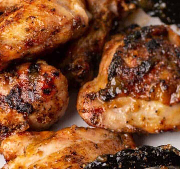A white platter full of grilled chicken drumsticks and thighs.