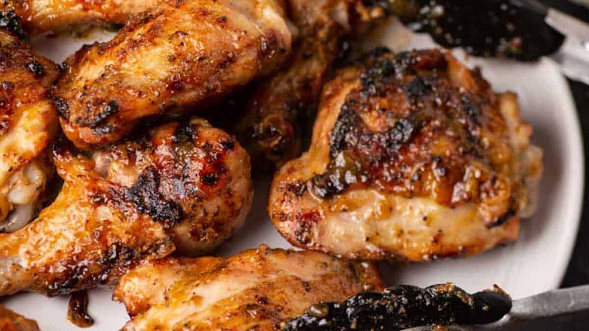A white platter full of grilled chicken drumsticks and thighs.