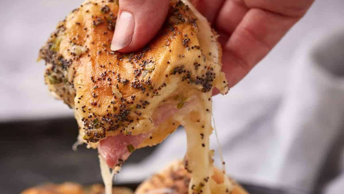 A Hawaiian roll slider being lifted from a platter.