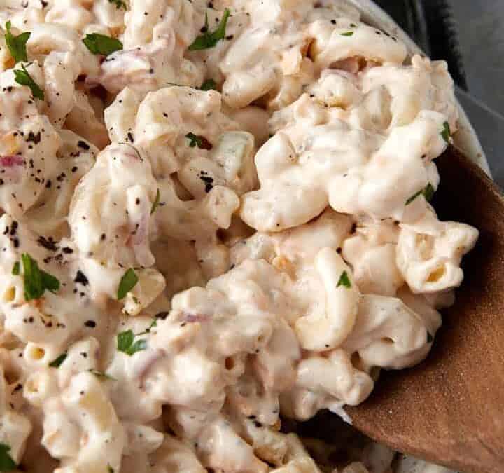 Creamy macaroni salad with a wooden spoon.