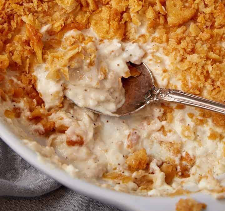 A serving spoon in a casserole dish of million dollar chicken.