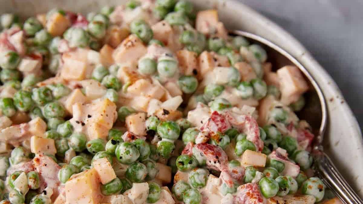 A bowl of pea salad with a serving spoon.