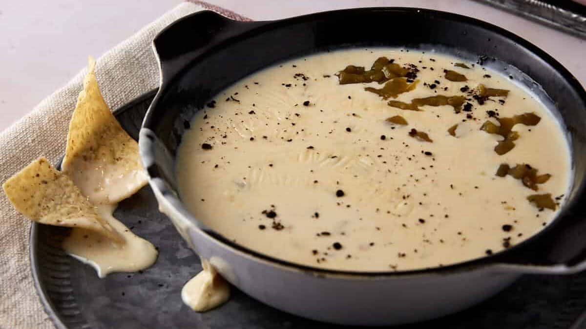 A bowl of white queso dip with chips on a plate.