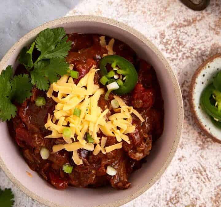 Three bowls of beef chili next to a soup ladel.