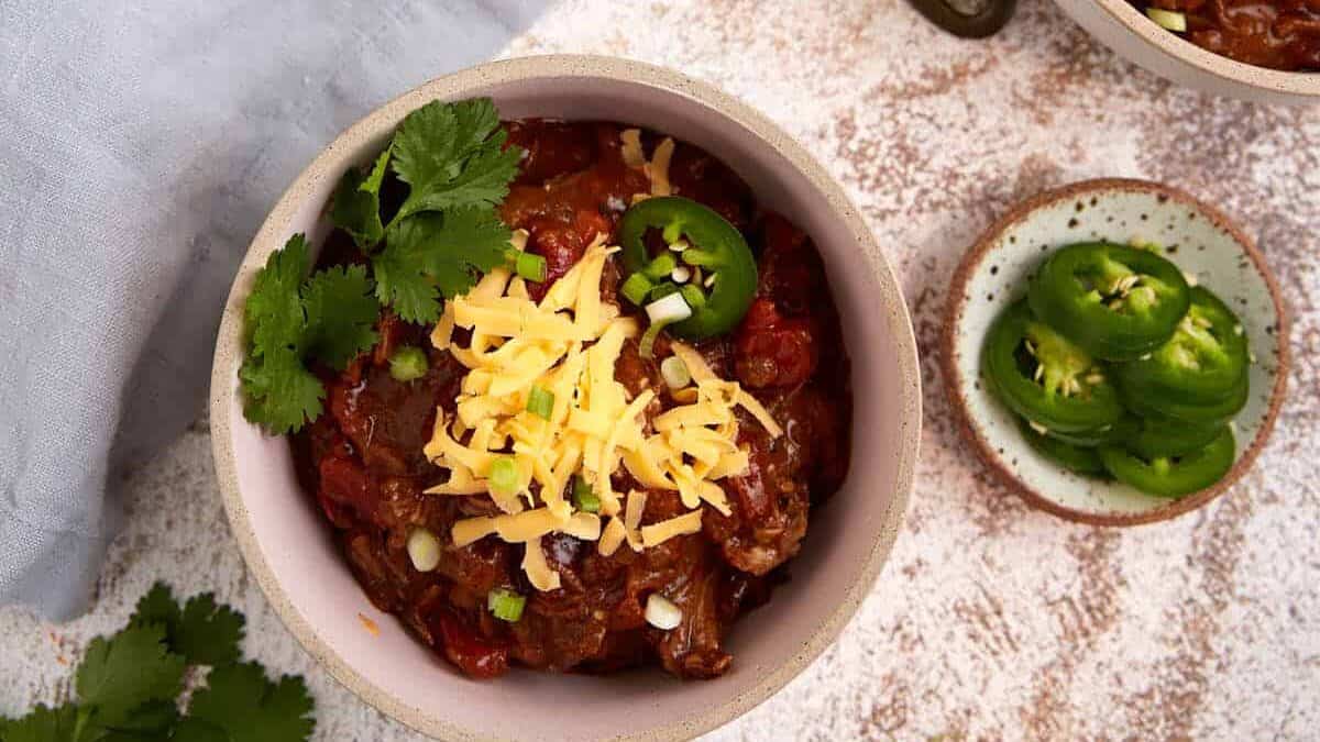 Three bowls of beef chili next to a soup ladel.