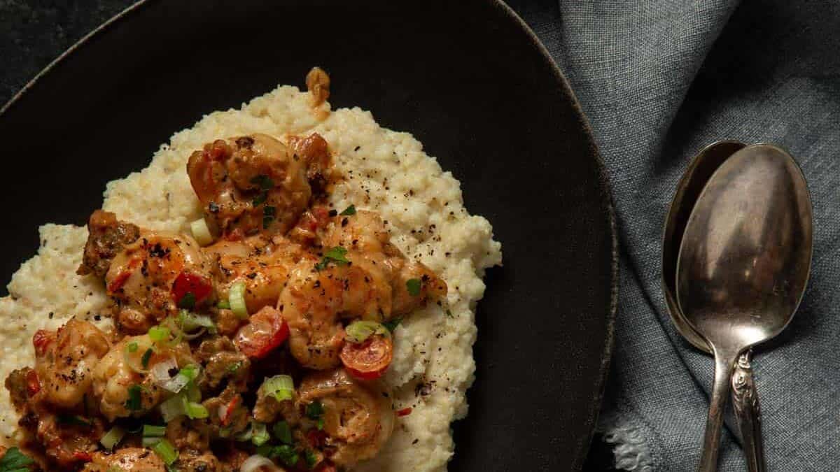 A black platter topped with creamy grits and shrimp and sauce.