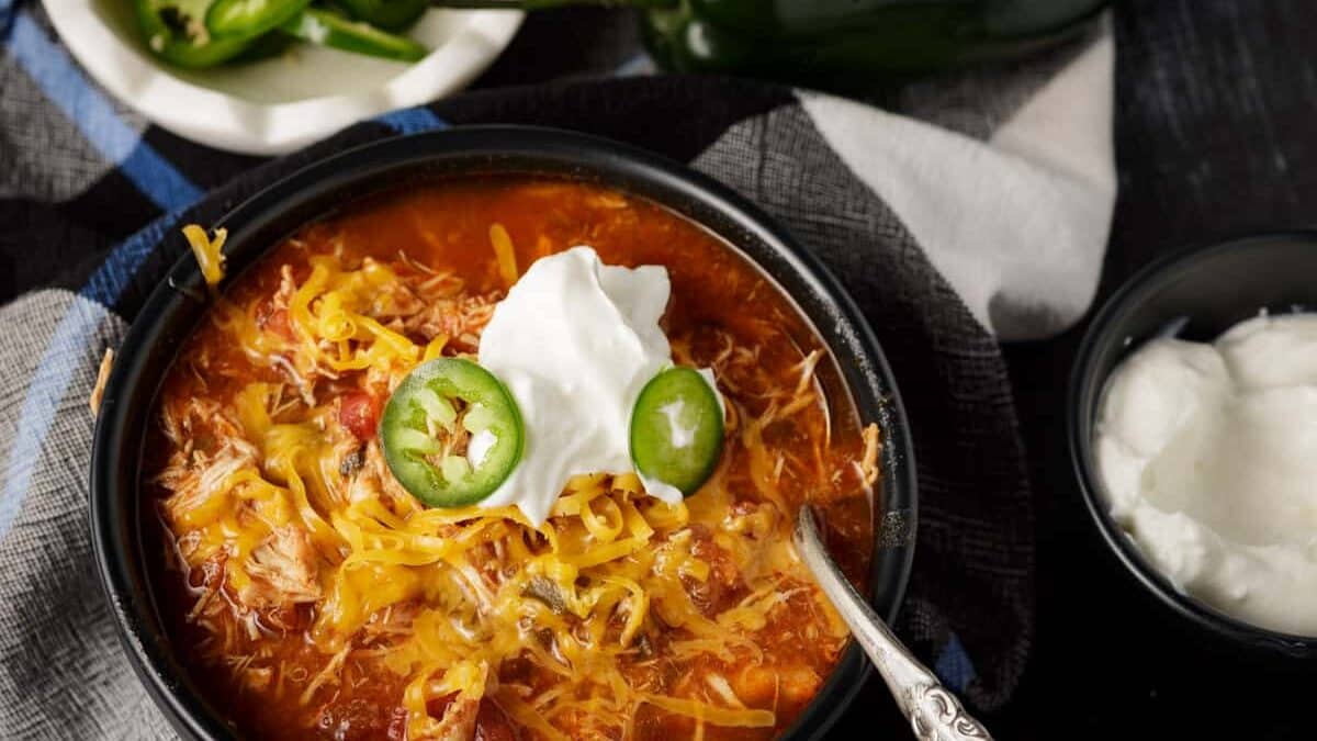 A bowl of chili made in a slow cooker topped with cheese and sour cream