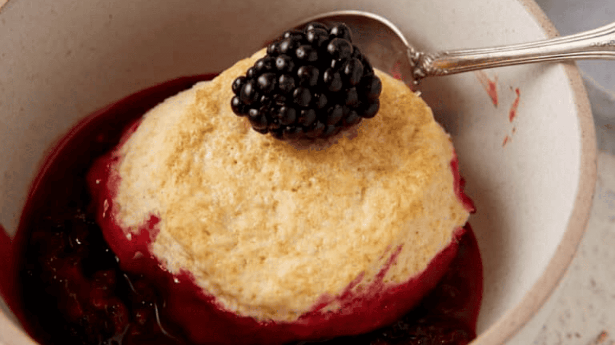 A bowl of dessert with blackberries and a spoon