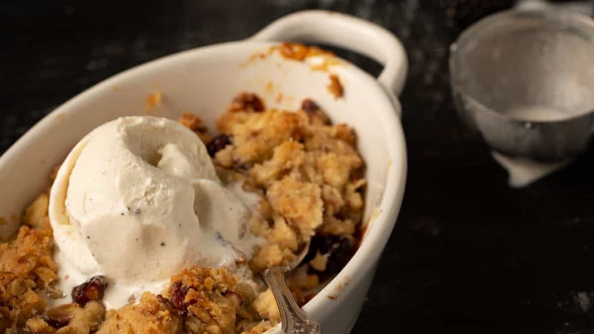 Two ramekins of apple blackberry crumble with an ice cream scoop and vanilla ice cream.