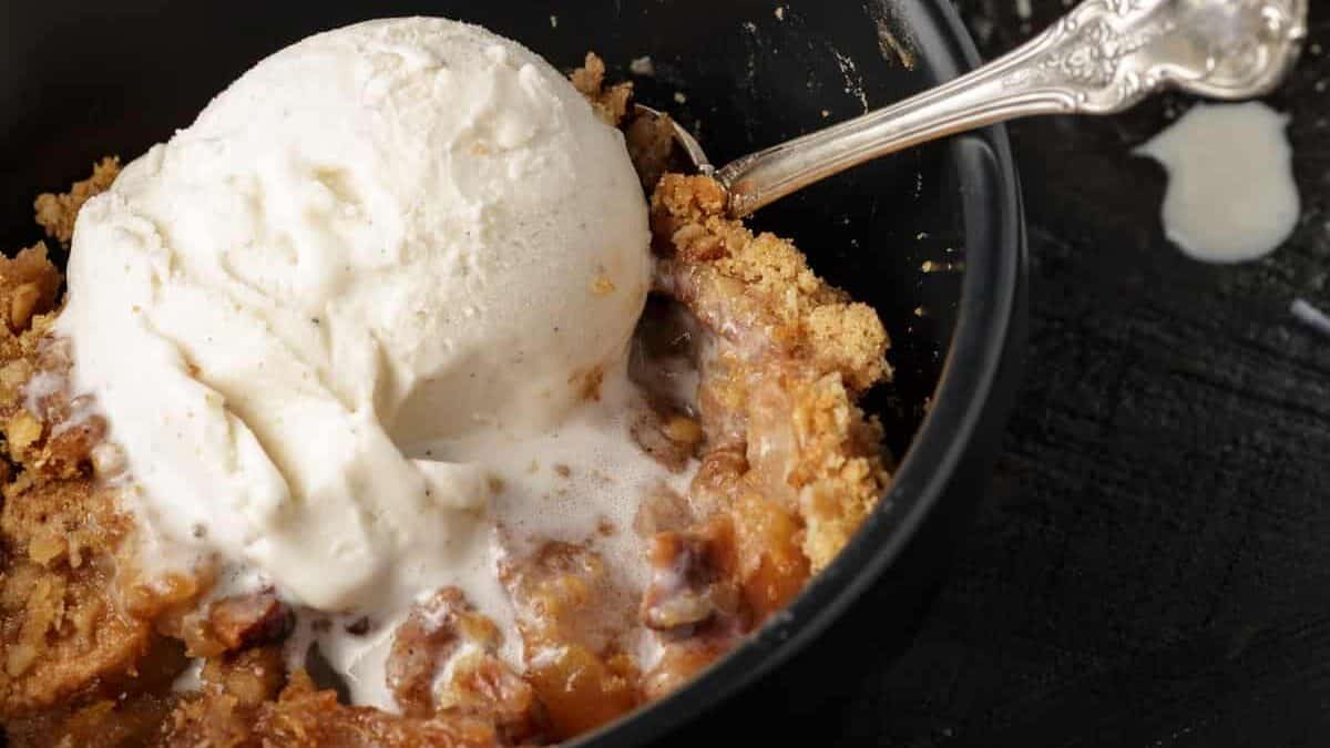 Apple crisp in a bowl with ice cream and a spoon