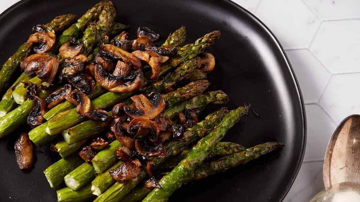 A platter of asparagus with mushrooms next to a container of balsamic vinegar