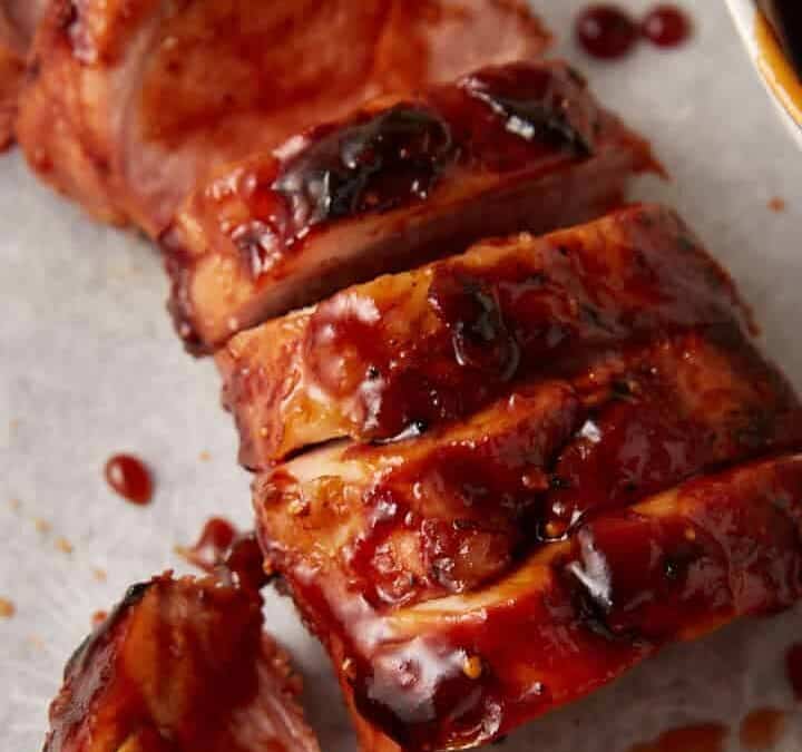 A pork tenderloin sliced and covered in bbq sauce.