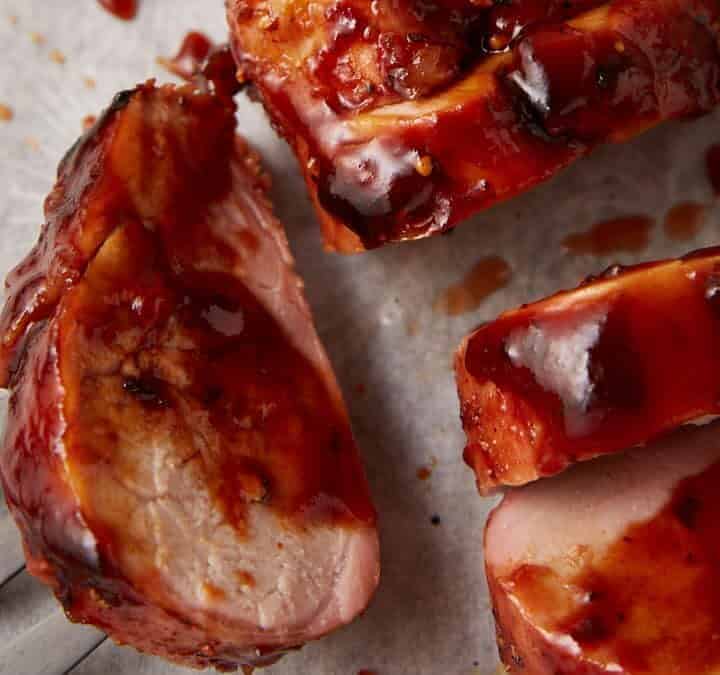 A pork tenderloin sliced and covered in bbq sauce.